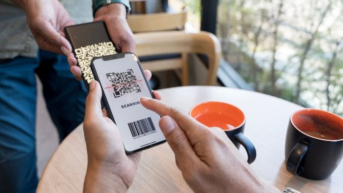 Zákazník skenuje QR kód, provádí rychlou a snadnou bezkontaktní platbu pomocí smartphonu v kavárně, muž držící smartphone při komunikaci s pracovníkem restaurace, aby provedl platbu.