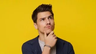 Mladý muž se zamyšleným výrazem kouká vzhůru s rukou pod bradou