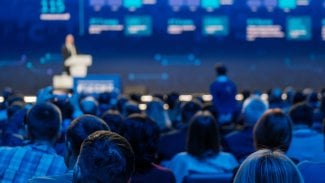 Soustředěné publikum na konferenci poslouchá řečníka na pódiu a vstřebává podstatu výměny znalostí.