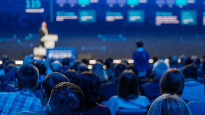 Soustředěné publikum na konferenci poslouchá řečníka na pódiu a vstřebává podstatu výměny znalostí.