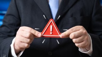 Muž v obleku drží v prstech výstražné znamení.