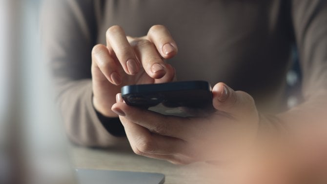 Detail prstů s nalakovanými nehty vyťukávající něco na displeji mobilu