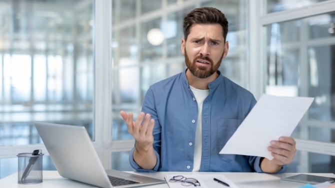 Muž v kanceláři drží v ruce papír a vypadá rozhořčeně