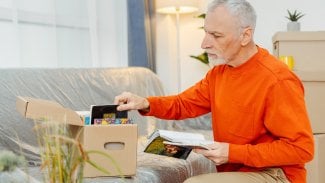 Starší muž v penzi se stěhuje, sedí v obýváků a třídí věci do krabice