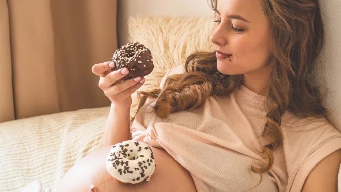 Těhotná mladá žena jí donuty s polevou