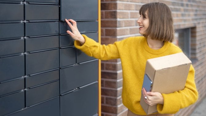 Výdejní box, u kterého stojí mladá žena s balíkem v ruce.
