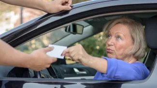 Starší žena sedící za volantem podává policistovi řidičský průkaz