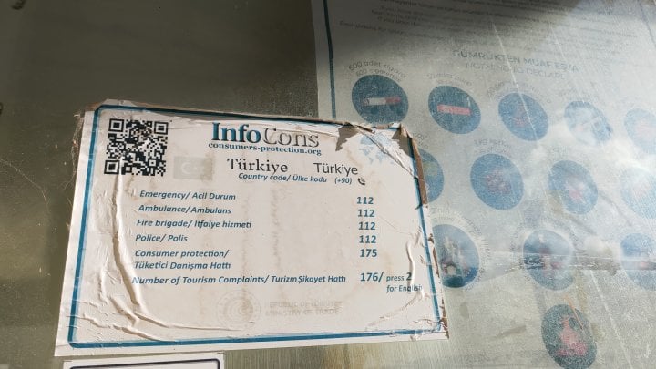 Nálepka s kontakty nouzových telefonních čísel v Turecku. QR kód vede na web consumers-protection.org, což je rumunský projekt. (13. 09. 2025)