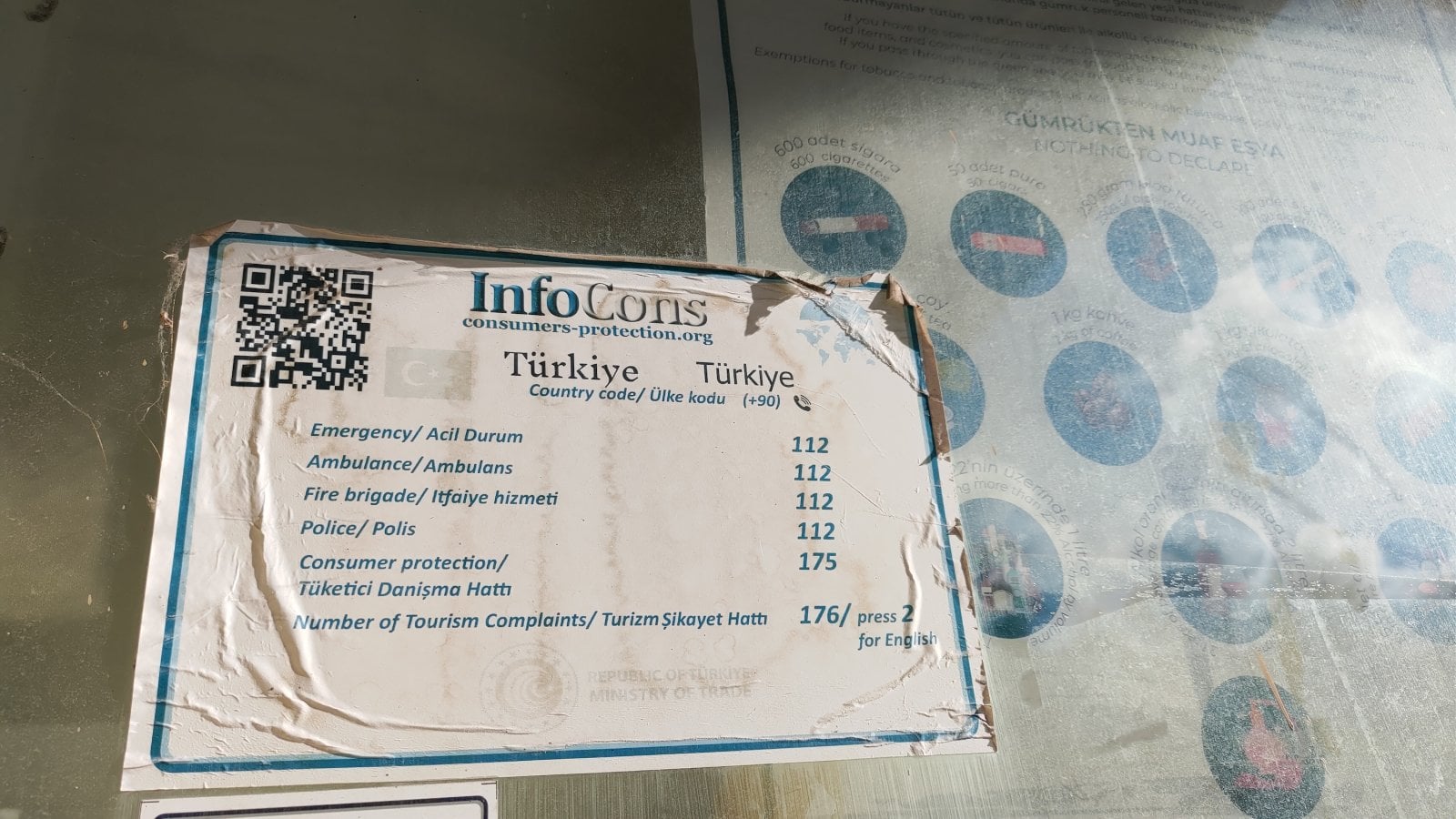 Nálepka s kontakty nouzových telefonních čísel v Turecku. QR kód vede na web consumers-protection.org, což je rumunský projekt. (13. 09. 2025)