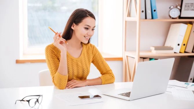 Usmívající se mladá žena sedí u počítače a prohlíží si monitor