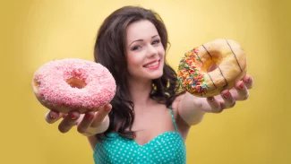 Tmavovlasá žena drží v rukou dva donuty