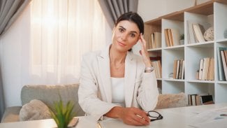 Zamyšlená hezká žena oblečená v kostýmku sedí u stolu v kanceláři