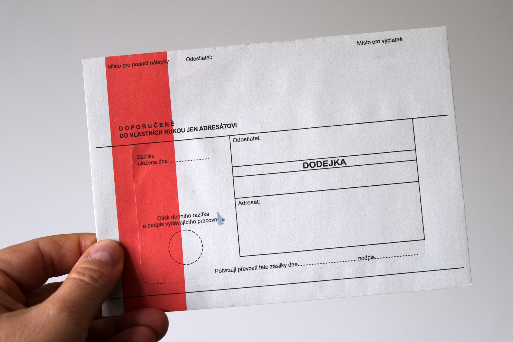 Ruka držící obálku s červeným pruhem.