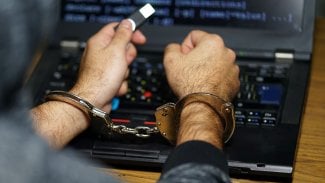 Zatčený hacker s pouty u svého notebooku