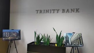 Logo TRINITY BANK na pobočce s květinami v truhlíku a obrazy na stojaně.