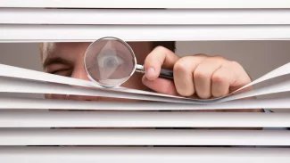 Šmírák pozoruje okolí přes žaluzie