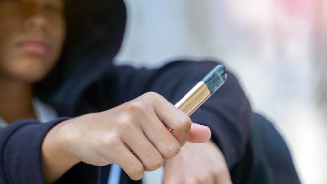 Kluk v mikině s kapucí drží elektronickou cigaretu