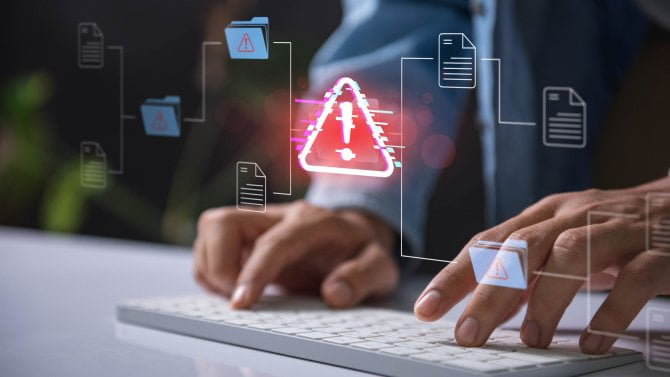 Ikona výstrahy upozornění s dokumentem hacknutým systémem.Ruční psaní na klávesnici s červeným výstražným signálem ohrožení kybernetické bezpečnosti obklopeným digitálními soubory a dokumenty.