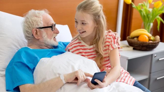 Mladá dívka sedí u staršího muže na nemocničním lůžku
