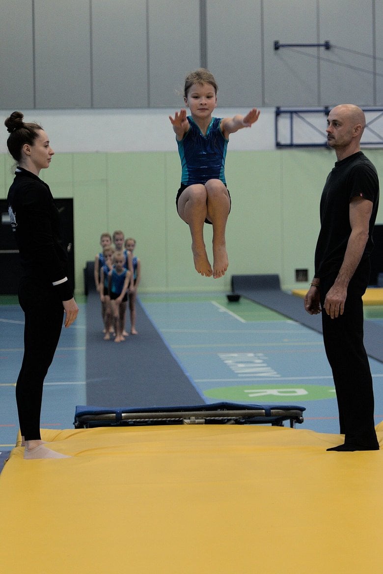 Tady je toho víc. Trenér se soustředí, cvičenka provedla skvělý cvik a usmívá se. Trenérka také ví, že se to povedlo. A vidíte i jemné napětí ostatních v týmu. (Pentax K-S2, 1/500s f/2,8 ISO1600)