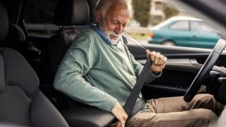 Senior sedí v autě za volantem a právě se připoutává