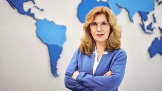Marianna Avalova se zkříženými rukami před mapou světadílů.