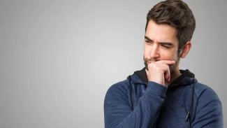 Mladý muž stojí s ustaraným výrazem, jednou rukou se drží za bradu